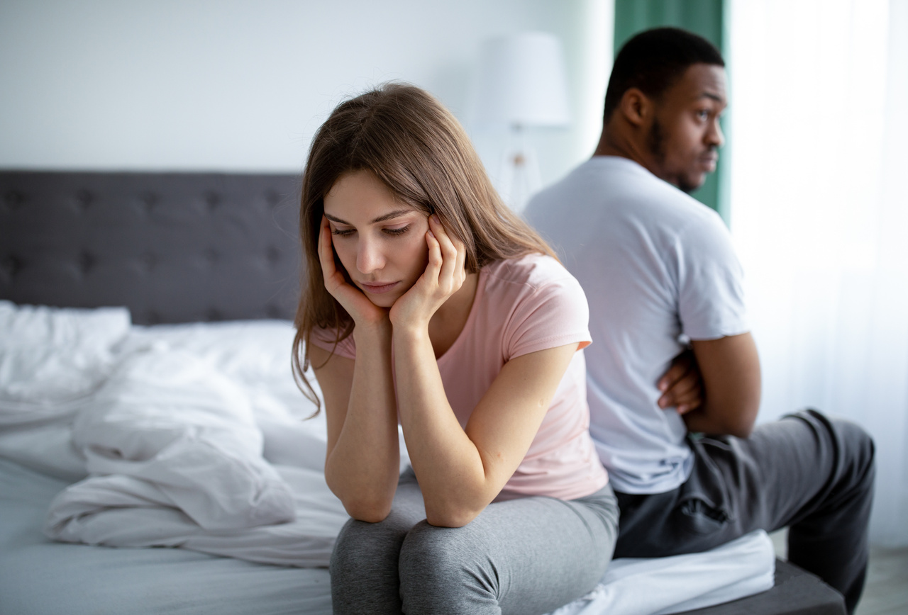 A couple turned away from each other, sitting on a bed